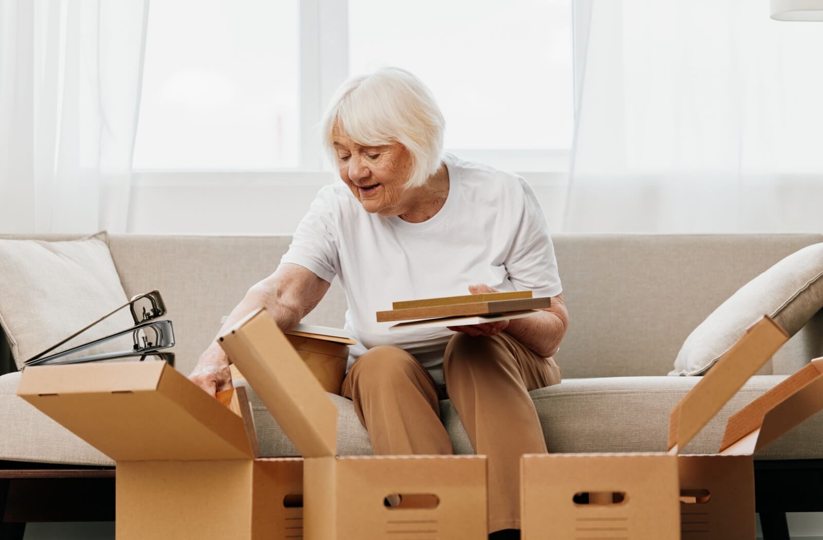 A senior packs some personal items into boxes while sitting on a sofa.