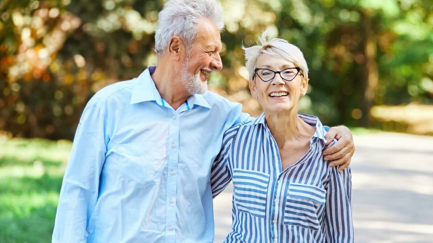 Two seniors enjoy a walk outside during a sunny day, since they no longer need to worry about home maintenance.